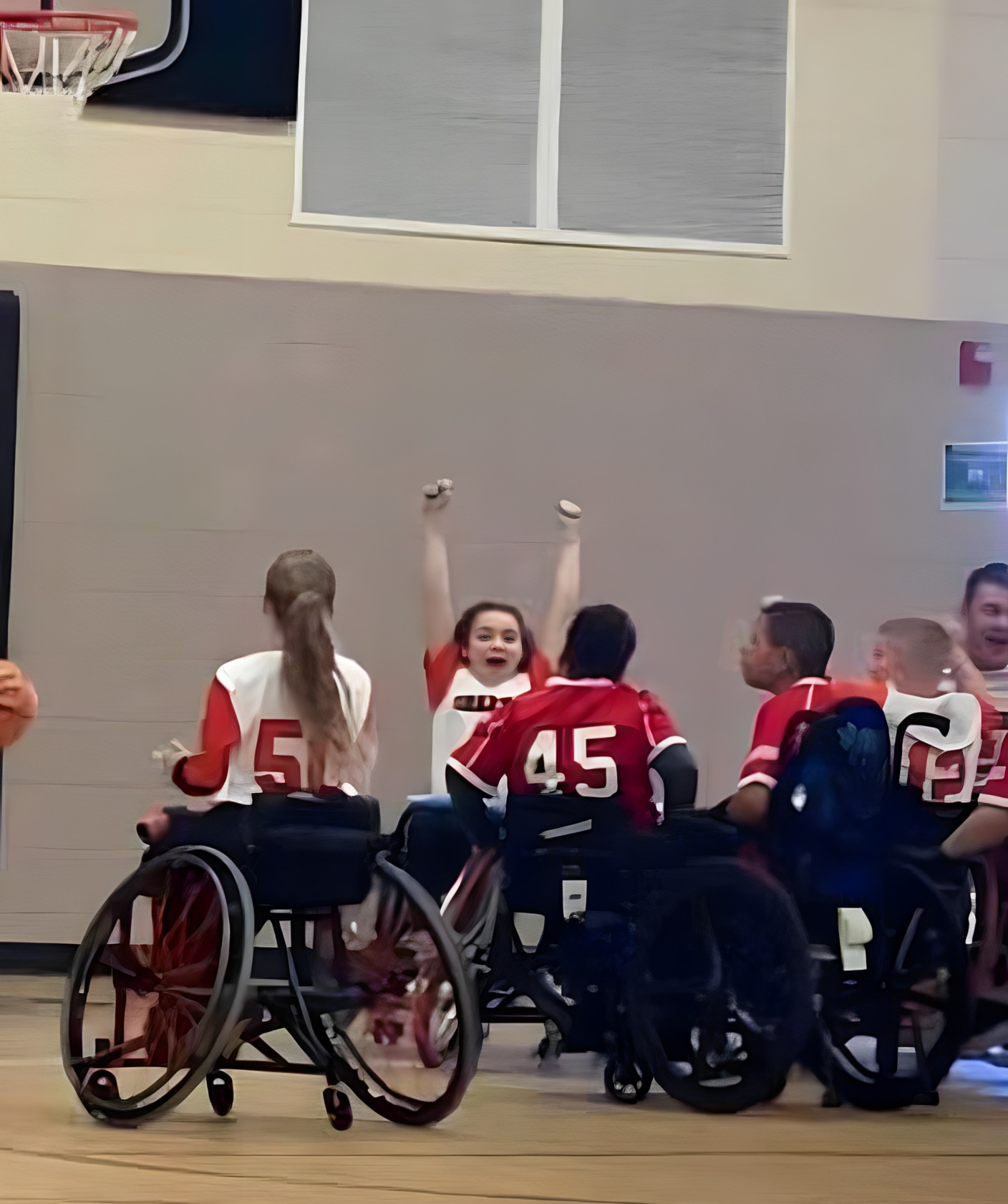 Adaptive sports Team of teens in wheelchairs in red ans white jerseys play on an indoor basketball court.