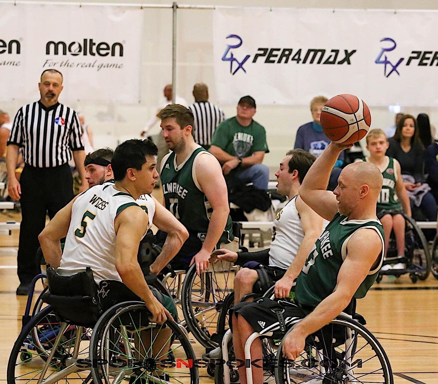 Adaptive sports: Group of teens wearing cleeveless team tank t-shirts in wheeldhairs on indoor basketball court packed tightly together trying to get the ball from one another