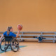 Adaptive sports: Teen with long blonde ponytail sitting in wheelchair on indoor basketball court holds basketball up in air in right hand