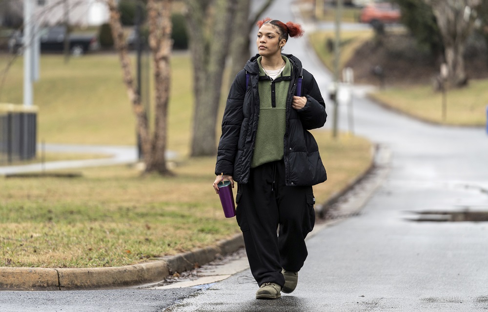 The pandemic missing; kids who didn't go back to school: black female student in large clothes walks down street with backpack and drink