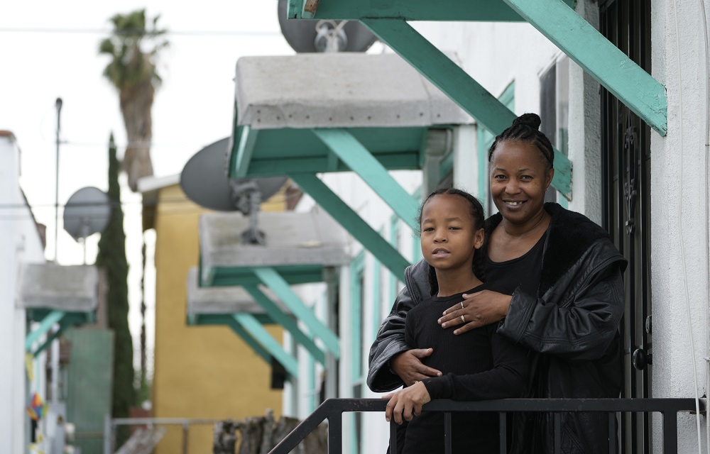 The pandemic missing; kids who didn't go back to school: black mother hugs her son from behind on front porch while smiling