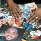 COVID families: Black woman's hands wearing a wedding ring lsort through several color photos overlapping laying on a table.