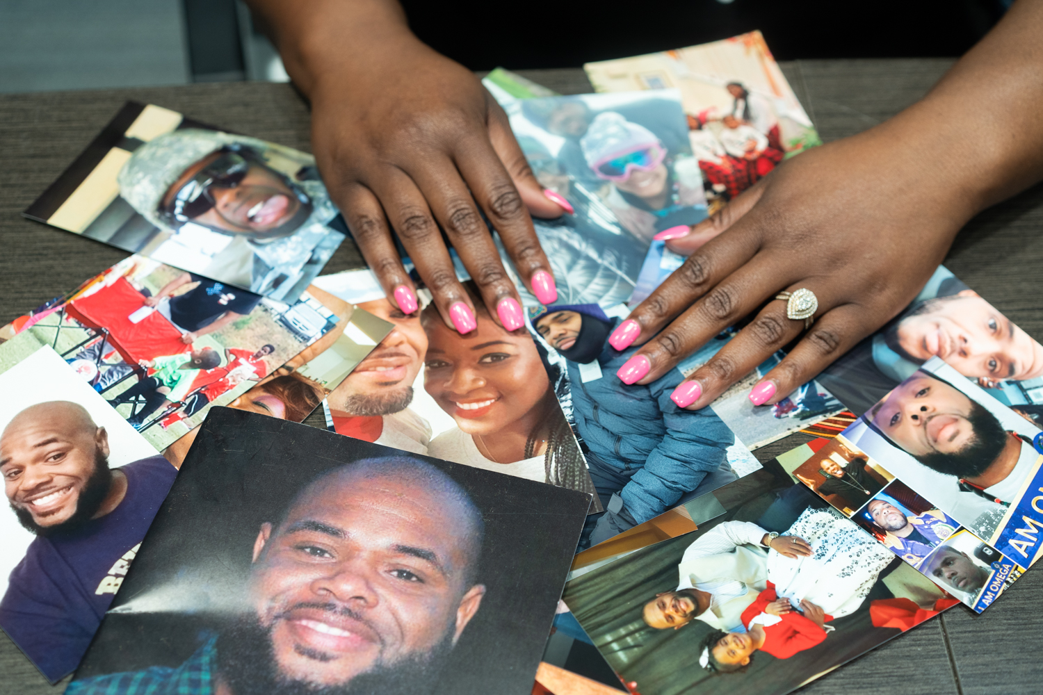 COVID families: Black woman's hands wearing a wedding ring lsort through several color photos overlapping laying on a table.