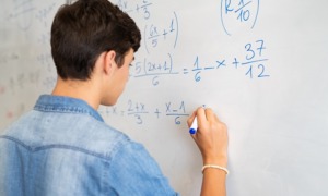 Math education improvement grants: male student in denim shirt doing math on whiteboard