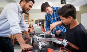 middle and high school STEM and financial literacy, education grant: young male teacher helping students working on tech project