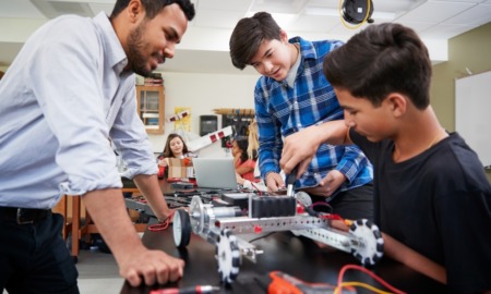 middle and high school STEM and financial literacy grants: young male teacher helping students working on tech project