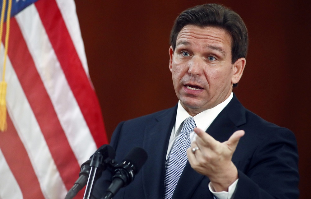 DeSantis to expand 'Don't Say Gay' law to all grades: white man with brown hair talking at podium while gesturing with hand