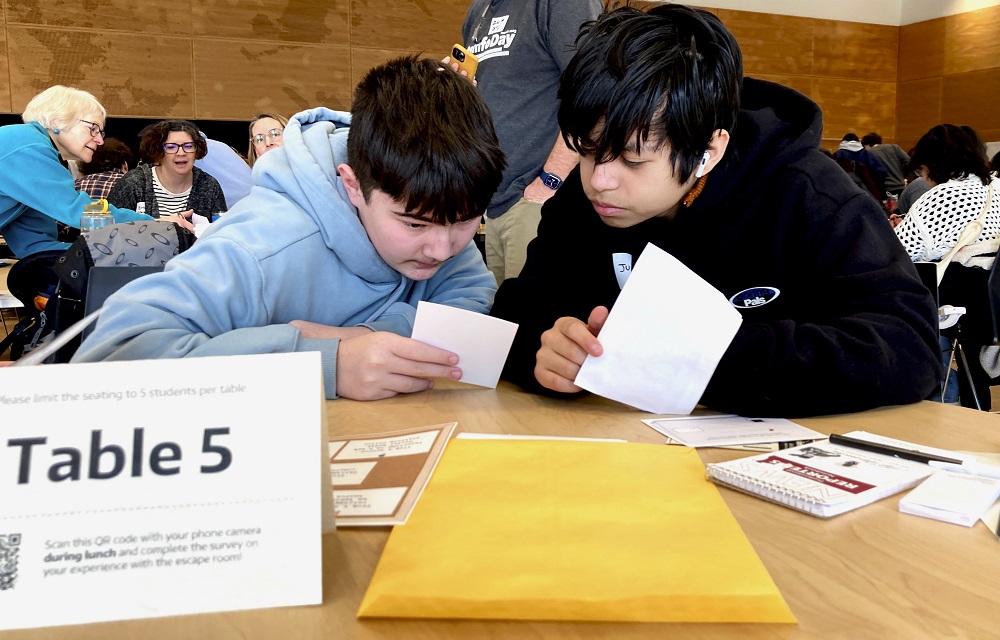 digital literacy, misinformation education: two young, male students looking at papers at table