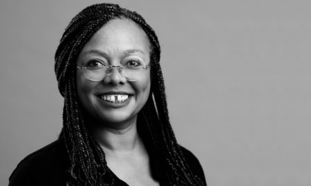 Holly Whitfield headshot: black woman with glasses and long hair in front of gray background