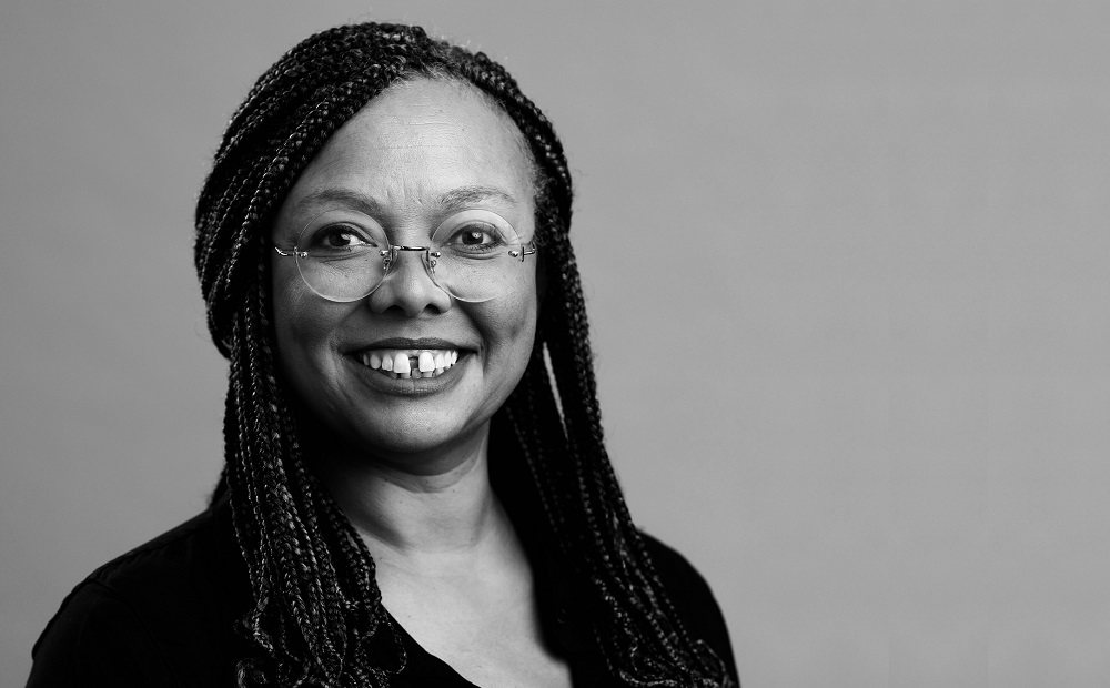 Holly Whitfield headshot: black woman with glasses and long hair in front of gray background