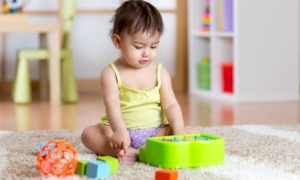 improving early childhood development outcomes grants: young child sitting on rug looking down at colorful toys