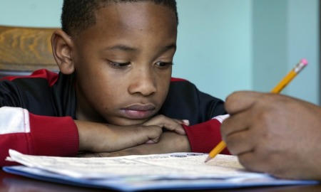 Many kids are struggling in school. Do their parents know?: young black boy stares at paper while someone points to it with pencil