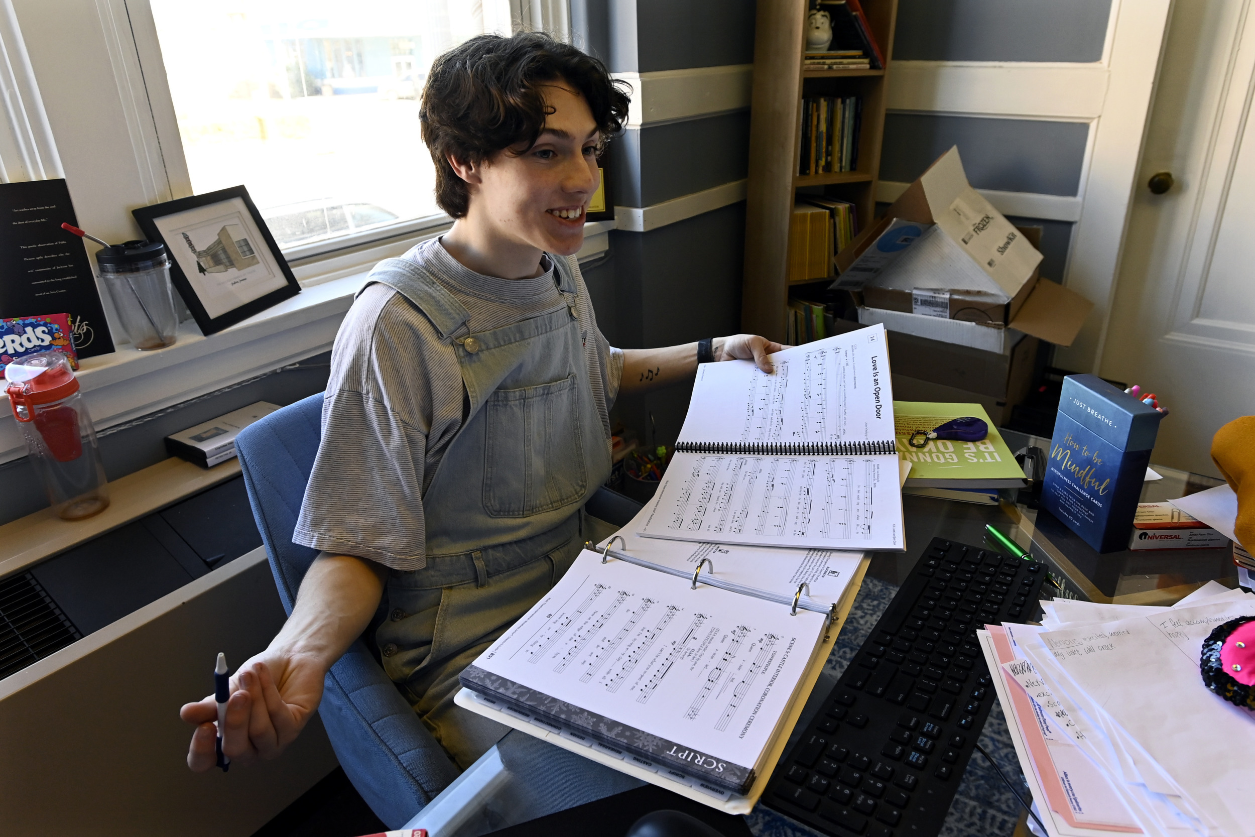 Skipping College: Dark-haired person in gray t-shirt sits at desk filled with open notebooks and papers