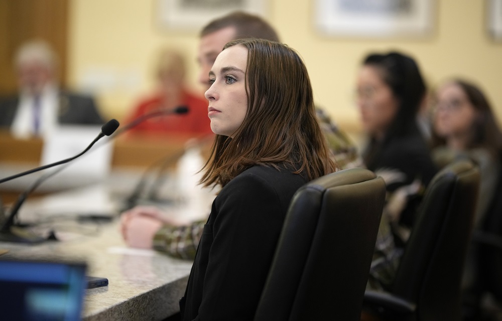 Surge in eating disorders spurs state legislative action: young woman with brown hair looks off to her left while seated at table with microphones
