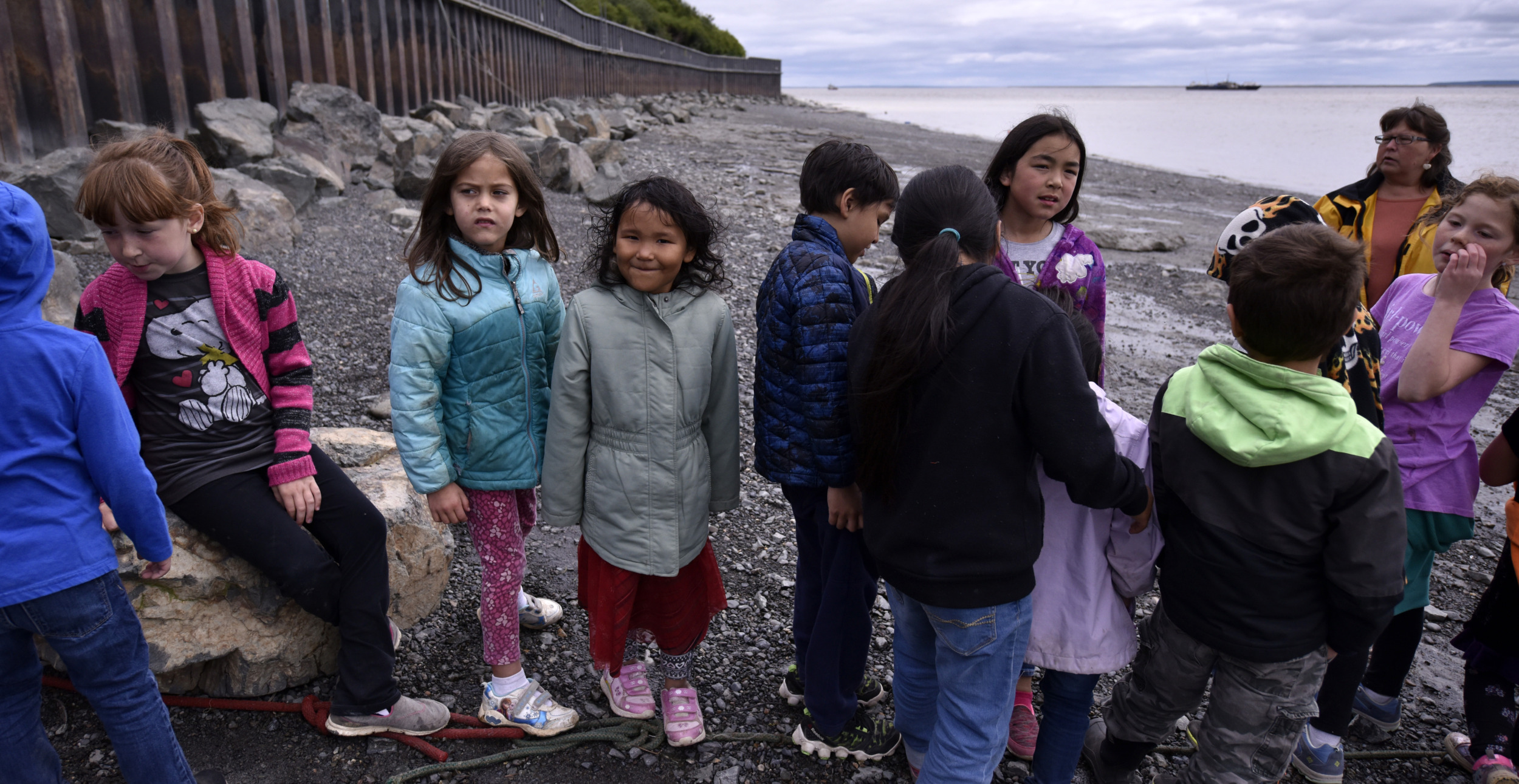 Native American afterschool programs: Several young children in winter coats stand with one adult on the shores of a lakeoutdoors
