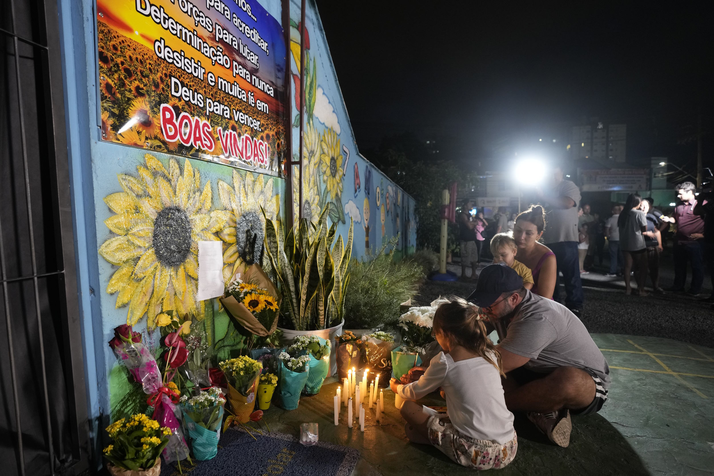 Brazil school violence: People crouch on siewalk laying flowers and lightng candle at a memorial for victims of school violence.