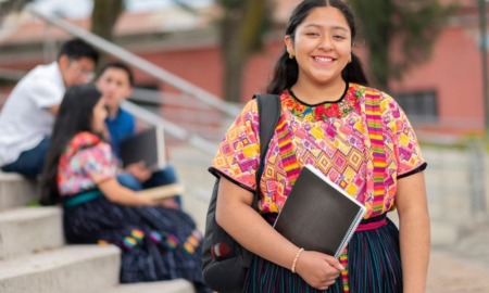 Native/tribal higher education student support grants: young native woman with backpack and notebook smiling on steps outdoors