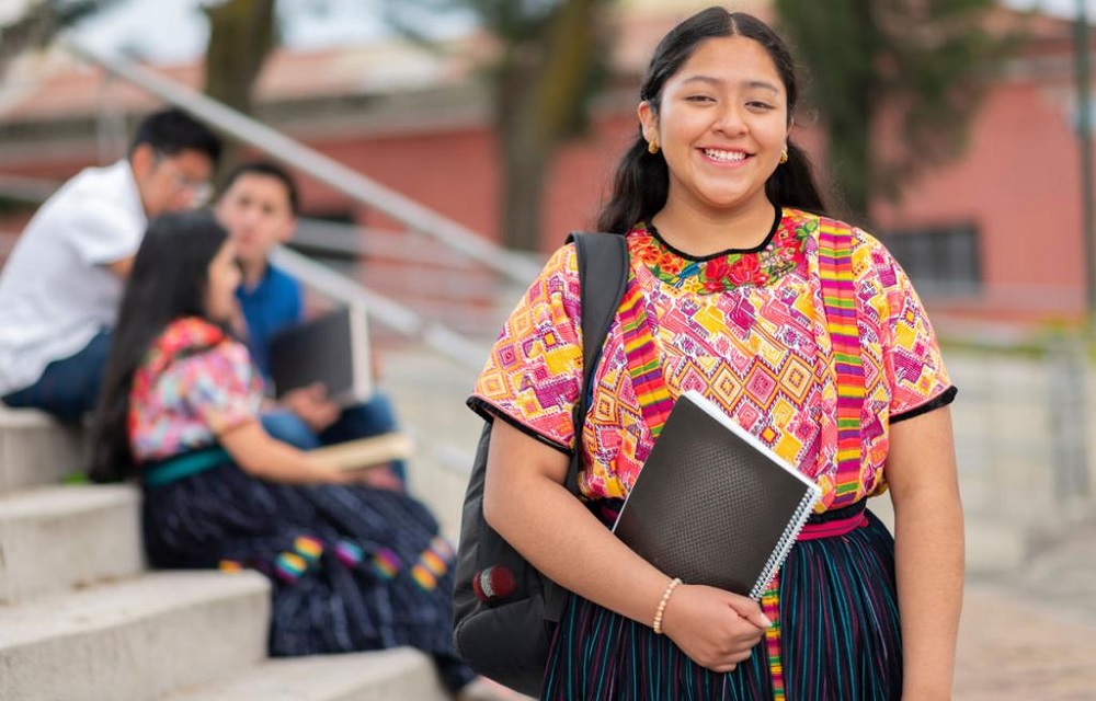 Native youth, tribal higher education student support grants: young native woman with backpack and notebook smiling on steps outdoors