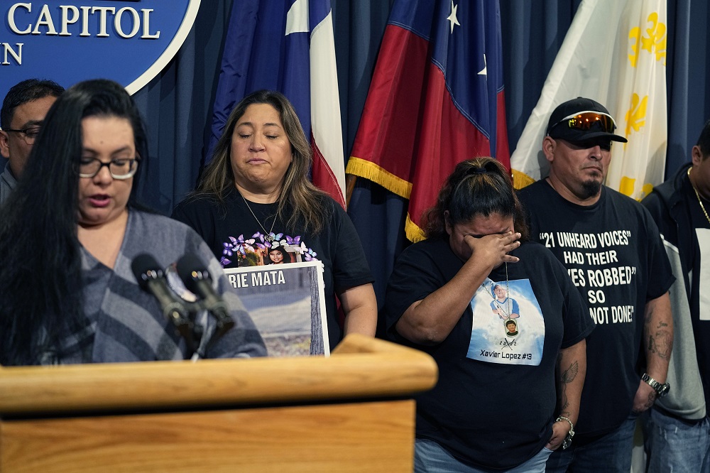 Uvalde families plead for languishing Texas gun bills: group of people in black shirts stand next to someone speaking at podium