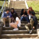 School start times: Six teen students sit on wide, long, outdoor, cement steps going up grassy hill.