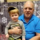 Family First program: older man in blue shirt holding smiling child wearing hat on lap