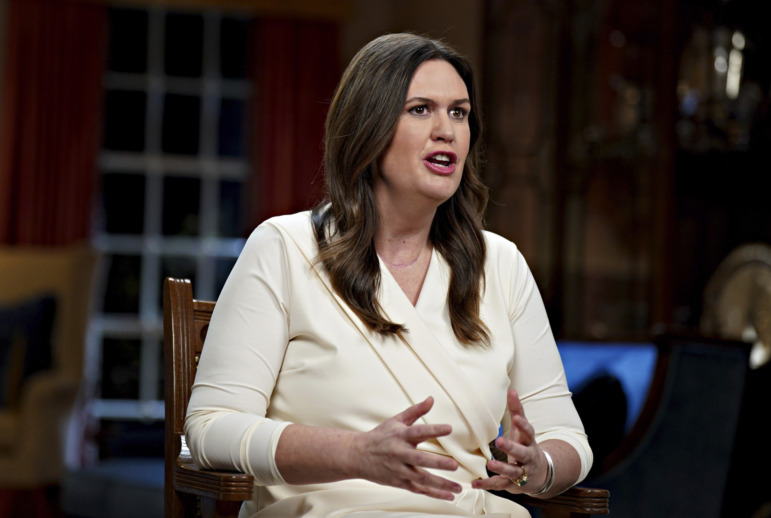 Child Labor Laws: Arkansas Gov. Sarah Huckabee Sanders, a woman with long dark hair in white dress, stands speaking and gesturing with hands.