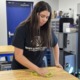 Teen workers in high demand for summer jobs: young woman in black shirt with long dark hair cleaning a table in workshop