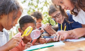 Condition of education report 2024: group of young students outdoors looking at something with magnifying glasses