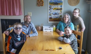 Families worry over future of medicaid caregiver payments: family sitting at wooden kitchen table smiling