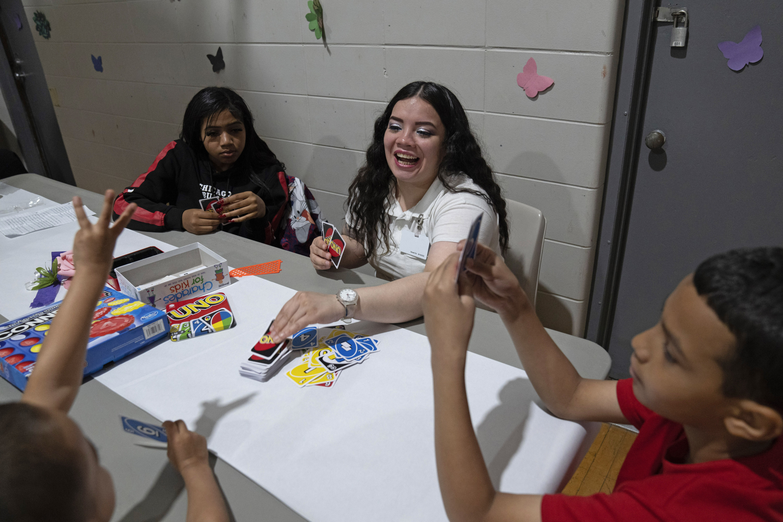 Reunification incarcerated parents: Adult woman with long, dark hair, and three children, sit at table covered with art supplies and games
