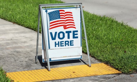 voting sign on sidewalk: "Vote Here" and American flag graphic on folding sidewalk sign