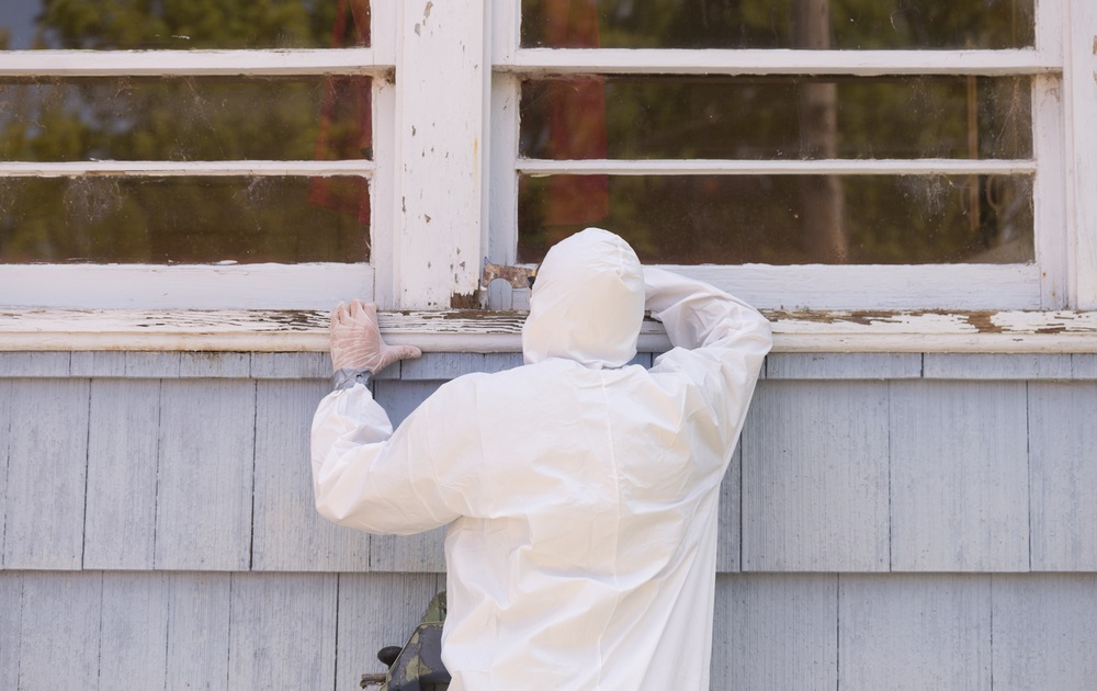 EPA proposes lower lead exposure limit in daycares, homes: person in hazmat suit painting the exterior window sill of older home