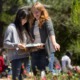 How states are using ESSER funds to strengthen high-quality OST learning: teacher with red hair teaching young Asian girl student outdoors by pointing at flowers