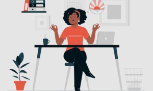 School mindfulness: Brown-skinned woman with curly black hair in black slacks and peach top sits behind table with laptop, eyes closed, elbows on desk and fingers of each hand forming a circle