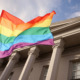 LGBTQ+ youth, students and Title IX: Rainbow flag closeup with traditional style, pillared building in the background