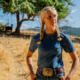 Goats - A person with two blonde braids wearing a blue t-shirt, jeans and a large belt buckle
