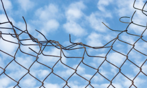 Young people lead us to a new vision of justice: Crushed top of chain link fence under blue sky with wispy clouds