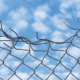 Young people lead us to a new vision of justice: Crushed top of chain link fence under blue sky with wispy clouds