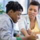 Job listing teacher-counselor: Black woman with short dark hair sits next to Black young adult with short braids reviewing paperwork in front of them.