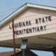 Juveniles in Angola Prison: Close-up of peaked, beige-siding roof over a drive-through entrance, with black lettering, "Louisiana State Penitentiary"