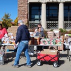Child poverty: Several people stand around outside in front of a brick building surrounding large tables stacked with packaged food - one man pulling a red wagon .