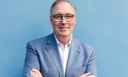 Tim Blaylock headshot: white man with dark-rimmed glasses in white shirt and blue blazer against light blue background