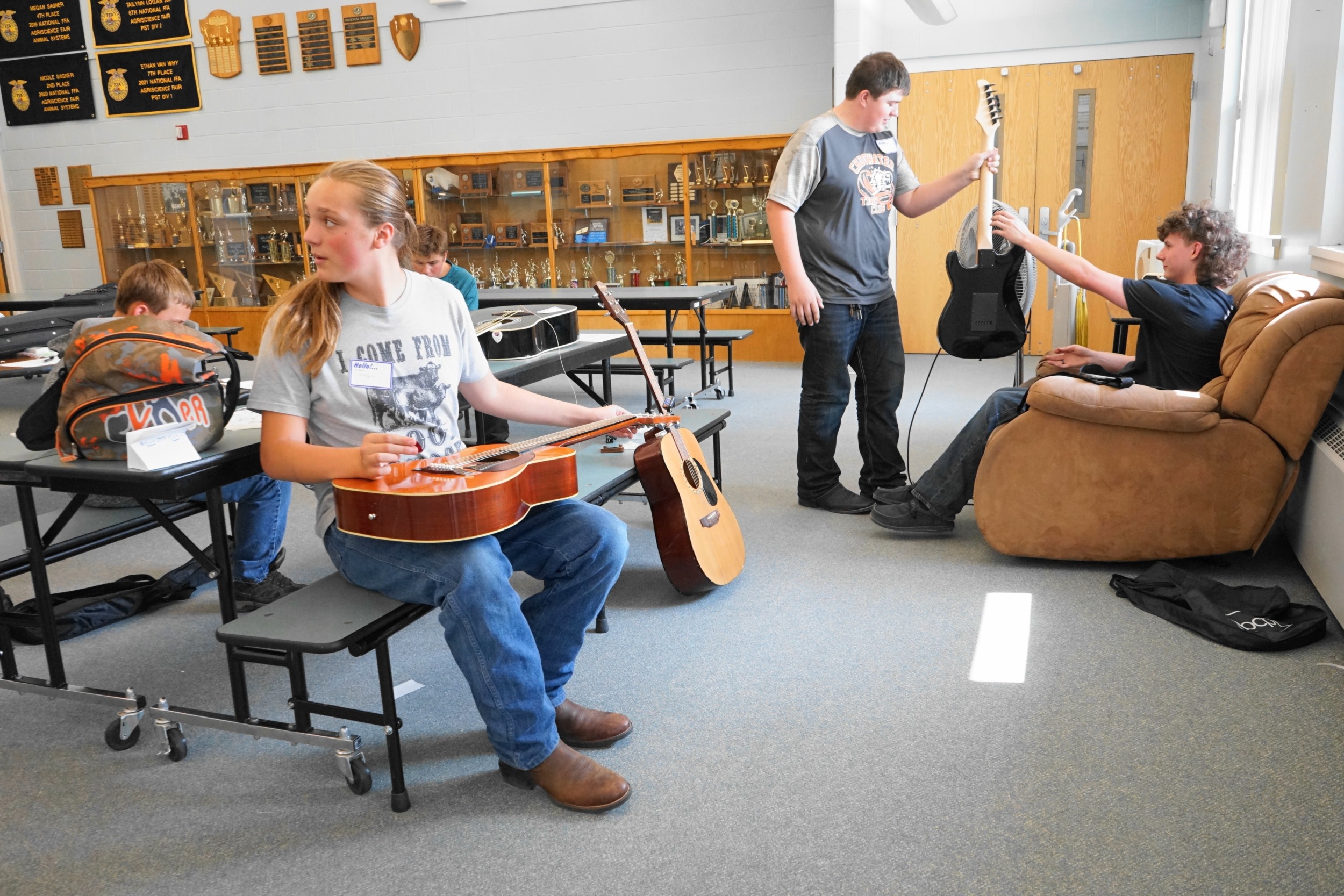 Chugwater, WY public school is now charter: students using guitars in a room with trophy cabinet in background