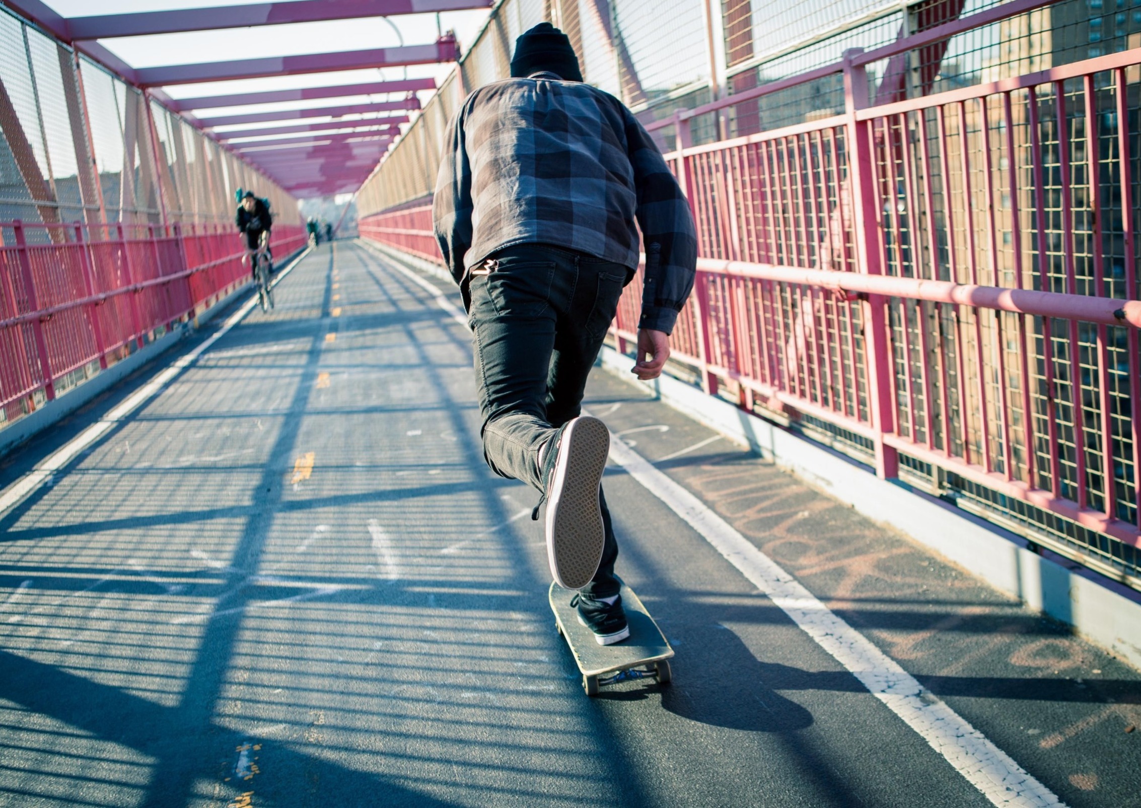 First-time juvenile offenders: Teen skateboarder in jeans and blue plaid shirt speeds through the pedestrian walkway on paved road over red metal bridge