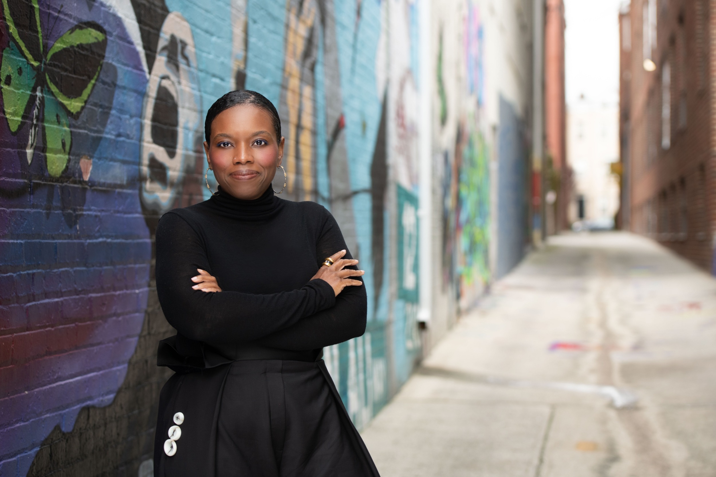 Candice Jones juvenile crime data: black woman wearing black standing in graffiti-ed alleyway with arms crossed
