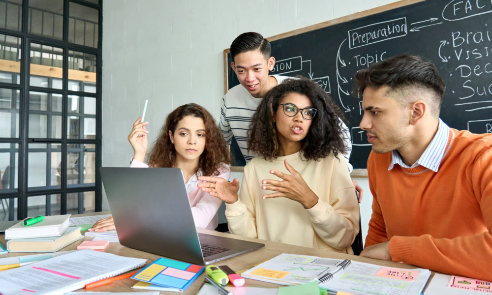 youth engagement, youth leadership, civic engagement: Four older students sit around laptop at table covered in multi-colored note papers in active discussion