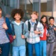 Happiness psychology: Line of happy teens stand with backpacks and book in front of a wall with floor to ceiling windows