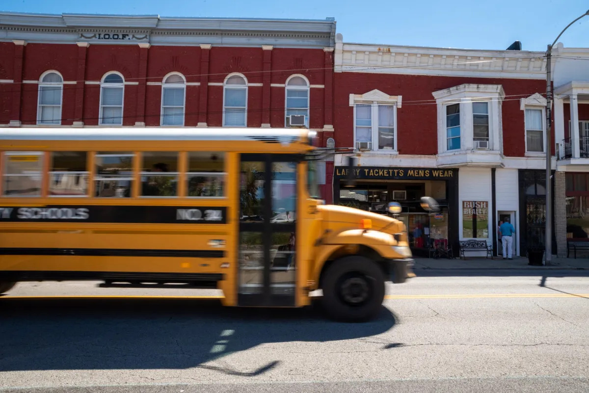 LGBTQ+ Clubs Kentucky: Yellow school bus drives in front of a two-story red brick building with white trim and small shops on ground floor.