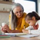 When grandparents raise grandkids: older woman with long hair holding coffee cup helping young girl with homework