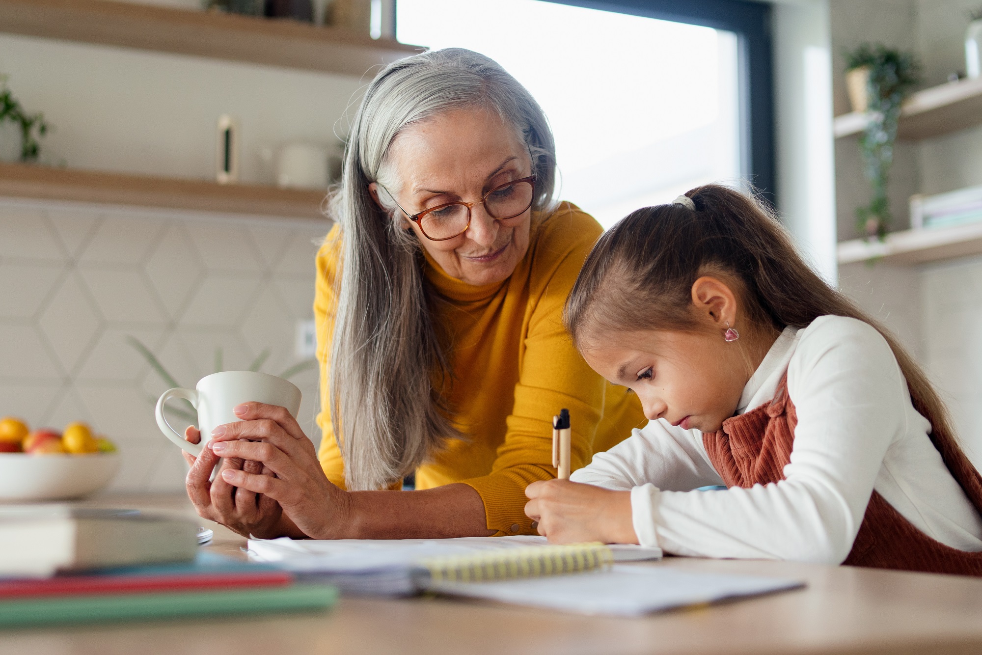 informal child care providers, When grandparents raise grandkids: older woman with long hair holding coffee cup helping young girl with homework